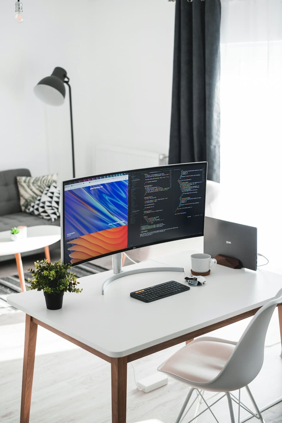 Monitor ultrawide e laptop su una scrivania moderna con pianta.