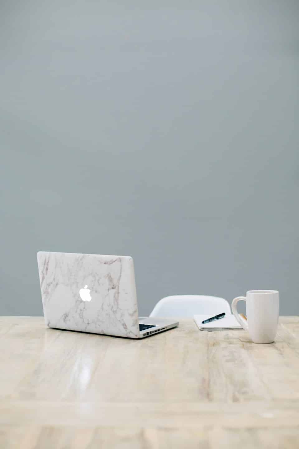 Laptop, taccuino e tazza di caffè su una scrivania di legno.